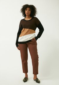 Striktrøje med sort, brun og hvid farveblokdesign; parret med brune, tilspidsede bukser og sorte, dekorerede slip-on sko.