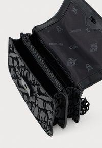 Bolso negro con un exterior liso y texturizado que presenta un diseño de letras en cursiva. Incluye dos compartimentos con cremallera y una correa de cadena.