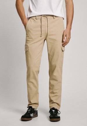 Pantalones cargo color caqui con cintura ajustable, bolsillos laterales y un corte relajado. Combinados con zapatillas negras con detalles en blanco.