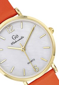 Montre en quartz doré avec un cadran texturé blanc, des index horaires dorés et un bracelet en cuir orange. Présente le nom de la marque "Go Mademoiselle."