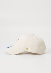 Beige pamut baseball sapka ívelt csúccsal, hímzett emblémával és oldalsó logóval kékkel és arannyal. Szellőzőlyukak találhatóak a tetején.