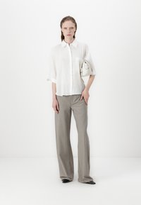 White short-sleeve button-up shirt with a pocket, paired with light gray tailored pants and black pointed-toe heels. Holding a small white bag.