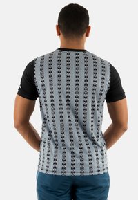 Camisa de manga corta con mangas negras. La parte trasera gris con un patrón presenta rayas verticales y logotipos circulares repetidos. Textura de tela suave.