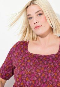 Lila blumengemustertes Kleid mit quadratischem Ausschnitt und kurzen Ärmeln. Es hat eine Mischung aus rosa und orange Tönen und besteht aus einem strukturierten Stoff.