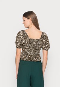 Blusa floral preta com mangas curtas balão. Apresenta uma parte traseira quadrada e uma textura franzida. Combinada com calças largas verde-escuras.
