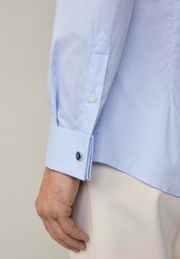 Lichtblauw gestreept overhemd met knoopmanchetten, voorzien van een gladde textuur en een contrasterende witte kraag met een enkele zwarte knoopaccent.