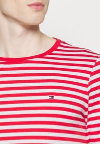 Rød- og hvidstribet langærmet t-shirt med rund hals og et lille broderet logo på brystet. 100% bomuldsstof, blød tekstur.