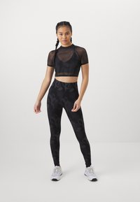 Top corto atlético negro con mangas de malla y leggins de cintura alta a juego que presentan un patrón abstracto tonal. Zapatillas blancas completan el conjunto.