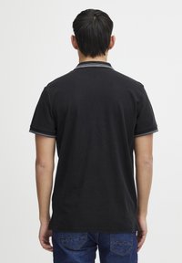 Svart polo skjorte med ensfarget design, med klassisk krage og stripete detaljer på kragen og ermene. Teksturen er glatt.