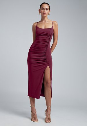 Mauve krāsas pieguļošs midi kleita ar sānu rumbu, plecu siksniņām un augstu šķēlumu līdz augšstilbam. Modelis apvienojis ar zelta siksniņu papēžiem.