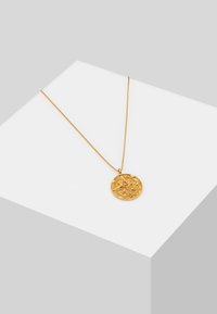 Collier en or avec pendentif rond présentant un motif d'étoile en relief, exposé sur une surface blanche avec un fond gris.