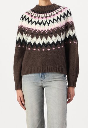 Bruine gebreide trui met roze, zwarte en witte zigzag- en stippenpatronen, gedragen met lichtblauwe spijkerbroek bij een staand persoon.