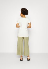 Camiseta branca de manga curta, de corte descontraído, combinada com calças largas verde-claro e sandálias pretas de plataforma com detalhes em prata. Fundo simples.
