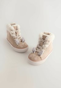 Beige kordbársony magas szárú cipők bolyhos béléssel és nyuszifülekkel. Varrott arcfelületek és lapos gumitalpak jellemzik.