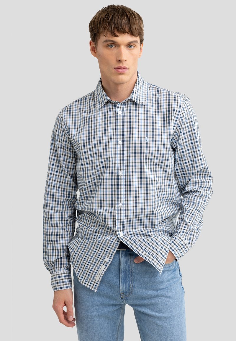 Gestreept overhemd in blauw en wit; lange mouwen, standaard kraag en lichtgewicht stof. Gecombineerd met lichtblauwe jeans.