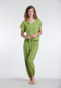 Un abbigliamento verde chiaro e dal taglio morbido presenta una maglietta a maniche corte con scollo a V e coulisse, abbinata a pantaloni elastici con vita in tinta.