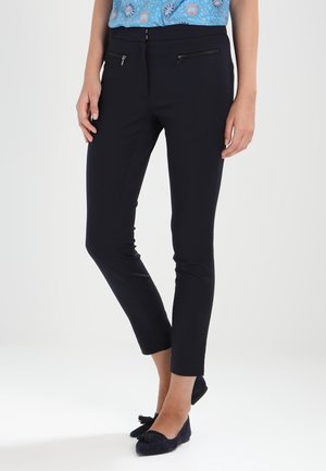 Marineblauwe stretchbroek met een slim fit, voorzien van twee voorkruispockets met rits en een gladde textuur. Verkorte lengte, aangevuld met platte schoenen.