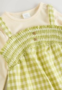 Vihreä ruudullinen mekko, jossa on smokkikuvioinen yläosa, puunapit ja vaalea päällikerros. Olkaimet ovat ruudulliset; kangas on pehmeä ja kevyet.