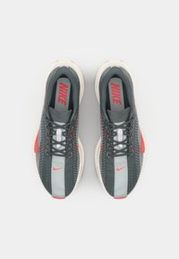 Baskets Nike avec une tige en mesh gris, des accents rouges et un design texturé. Lacets plats, semelle rembourrée et logo sur la languette.