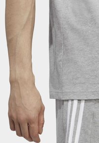 Camiseta de algodón gris con mangas cortas y cuello redondo, combinada con pantalones cortos grises que presentan tres rayas blancas en el lado.