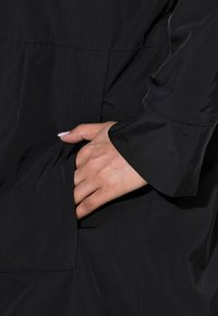 Svart vattentålig jacka med sidficka, len textur, långa ärmar och en skräddarsydd passform med subtila sömmar.