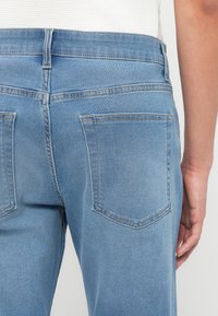 Πίσω όψη ατόμου που φοράει ουδέτερα μπλε τζιν παντελόνια με ορατές πίσω τσέπες και μέρος λευκού υφασμάτινου τοπ.