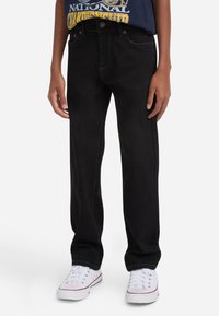 Jeans de denim negro con corte recto, cinco bolsillos y costuras en contraste, combinados con zapatillas blancas de corte bajo.