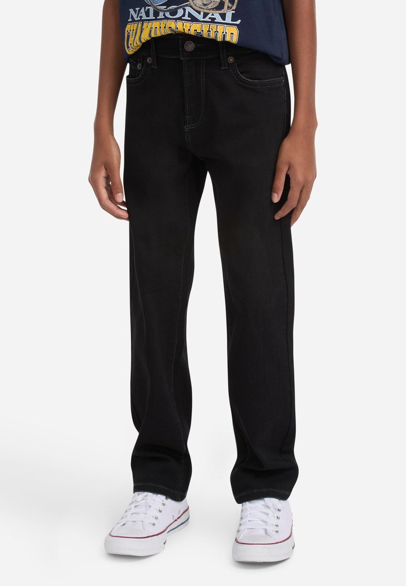 Jeans de denim negro con corte recto, cinco bolsillos y costuras en contraste, combinados con zapatillas blancas de corte bajo.