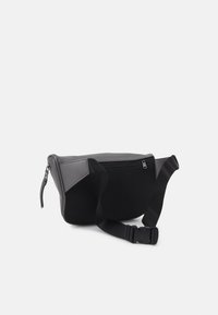 Czarna i szara torba wykonana z teksturowanego materiału, wyposażona w zamknięcie na zamek błyskawiczny oraz regulowany pasek dla wygody noszenia.