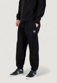 Schwarze Jogginghosen aus weichem Stoff, mit einem elastischen Bund, seitlichen Taschen und einem kleinen EA7-Logo-Patch am Oberschenkel.