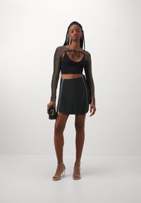 Fekete bordázott crop top, hosszú, csillogó ujjal párosítva, fekete mini szoknyával, amelyen ezüst cipzárak vannak az oldalán, és átlátszó, pántos magassarkúkkal.