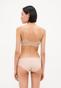 Bralette wireless beige con spalline regolabili e slip hipster coordinati con bordi ondulati, texture liscia e design minimalista.