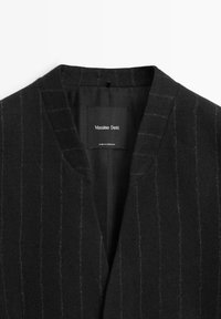 Czarna wełniana marynarka z dekoltem w serek, ozdobiona subtelnymi pionowymi paskami. Na wewnętrznej metce widnieje napis "Massimo Dutti", wskazujący producenta.