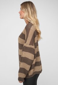 Brun og beige stripet genser med lange ermer, strikket tekstur, løs passform og ribbestrikkede mansjetter, vist fra siden.