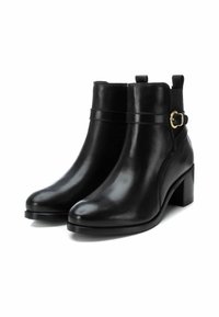 Botas de piel negra hasta el tobillo con punta redondeada, tacón de bloque de altura media y un acento decorativo de hebilla en una correa alrededor del tobillo.