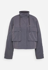 Cropped jacket in dark gray fabric, featuring two front pockets, a high collar, and drawstrings for adjustments. Smooth texture and relaxed fit.