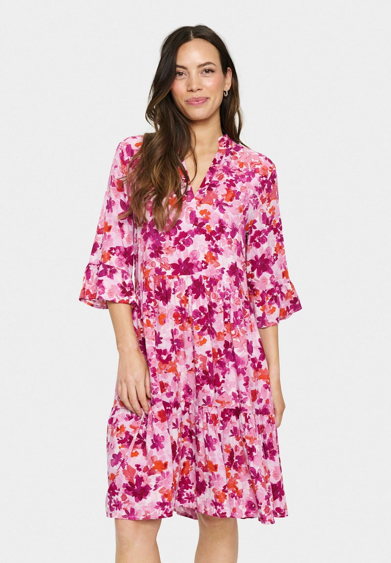 Blommig klänning i varierande nyanser av rosa och orange, med V-ringning, trekvarts bjällersleeve och tjock nederdel. Tillverkad av lätt tyg.