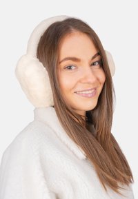 Cache-oreilles en fausse fourrure blanche avec des coussinets ronds et moelleux et un bandeau assorti, associés à une veste en tissu doux de couleur claire coordonnée.