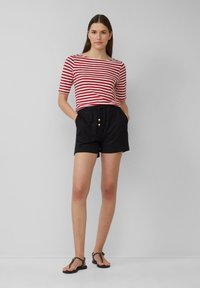 Rood-wit gestreepte t-shirt met korte mouwen, gecombineerd met zwarte shorts met een elastische tailleband en houten knopen. Zwarte sandalen maken de outfit compleet.