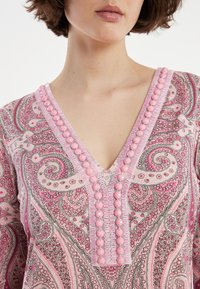 Rosa Tunika mit Paisleymuster, die einen V-Ausschnitt hat und mit rosa Perlen sowie kunstvollen Konturen verziert ist. Weicher Stoff und leichtes Material.