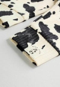 Manga de suéter de algodón con un patrón de estampado de vaca en colores negro y crema. Presenta canalé texturizado y una etiqueta con un gráfico de leche.