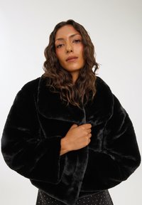 Cappotto cropped in finta pelliccia nera con ampio colletto e maniche oversize, caratterizzato da una texture morbida e una vestibilità rilassata.