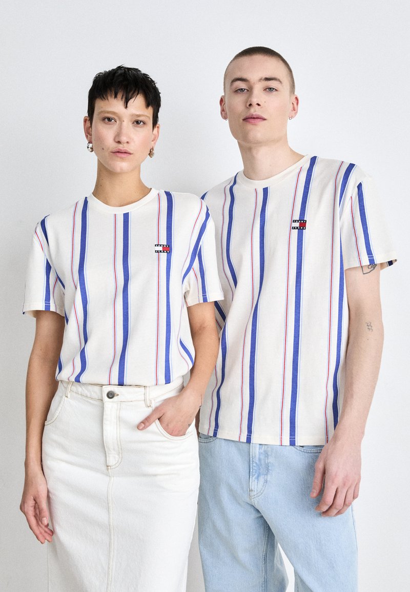 T-shirts rayés en crème, avec des lignes bleues et rouges, arborant un petit logo. Assorti avec une jupe en denim blanche et un jeans bleu clair.