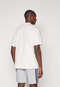 Vit t-shirt med kort ärm och avslappnad passform. Tillverkad i bomull, med enkel design och rundad halsringning. Parat med gråa shorts med sidostrikar.