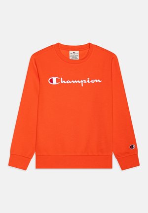 Sweat-shirt orange à manches longues avec le logo texte « Champion » en blanc sur la poitrine et un petit patch logo sur le poignet de la manche gauche.