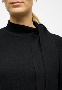 Czarny sweter z wysokim kołnierzem i drapowanym akcentem z materiału. Teksturowany materiał o gładkim wykończeniu. Zbliżenie na detale dekoltu.