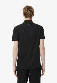 Svart polo skjorta med geometriskt mönster, korta ärmar och kontrasterande krage. Guldiga detaljer på nacken och ärmen. Lättviktig tyg.