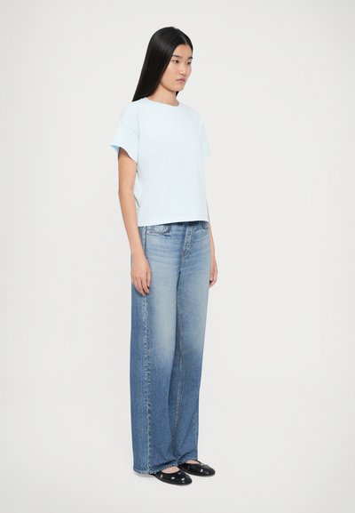 Lys blå t-shirt med en afslappet pasform og korte ærmer, parret med brede, falmede blå jeans, afsluttet med sorte flade sko.