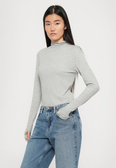 Gray long-sleeve mock neck top with a fitted design, worn with loose blue denim jeans. Soft texture, minimalistic style, no visible patterns.