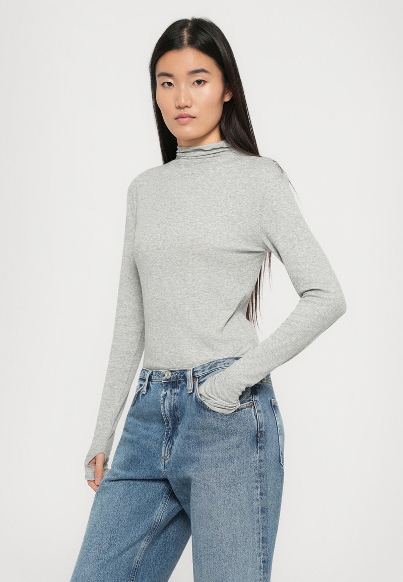 Grauer langärmeliger Top mit Mock-Neck und körperbetontem Design, kombiniert mit lockeren blauen Jeans. Weicher Stoff, minimalistischer Stil, keine sichtbaren Muster.